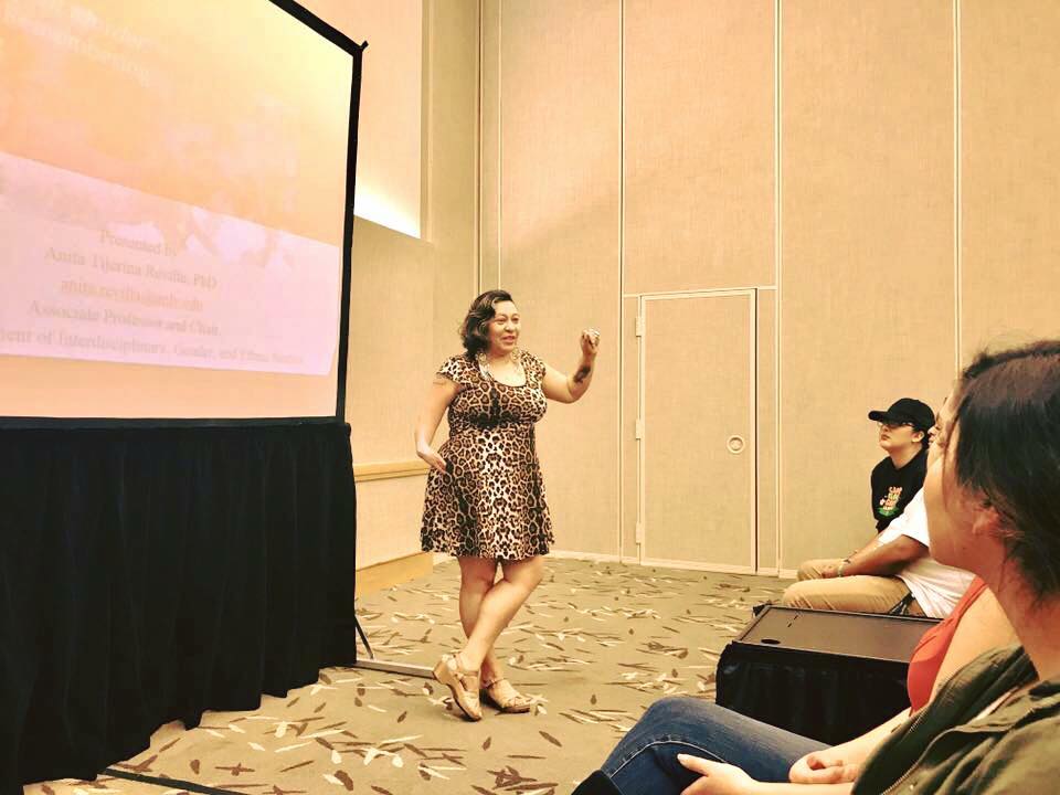 Anita is lecturing in a room with a screen behind her.